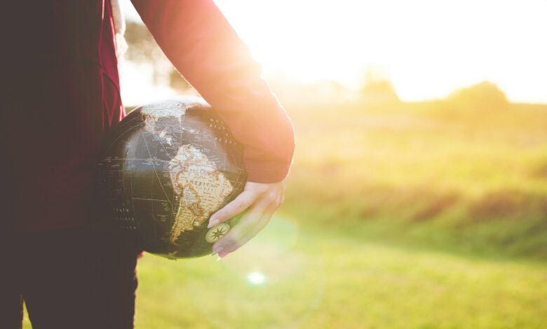 person holding black and brown globe ball while standing on grass land golden hour photography